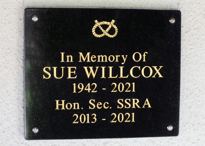 Photograph shows the memorial plaque mounted on the clubhouse wall, dedicated to Sue Willcox.
