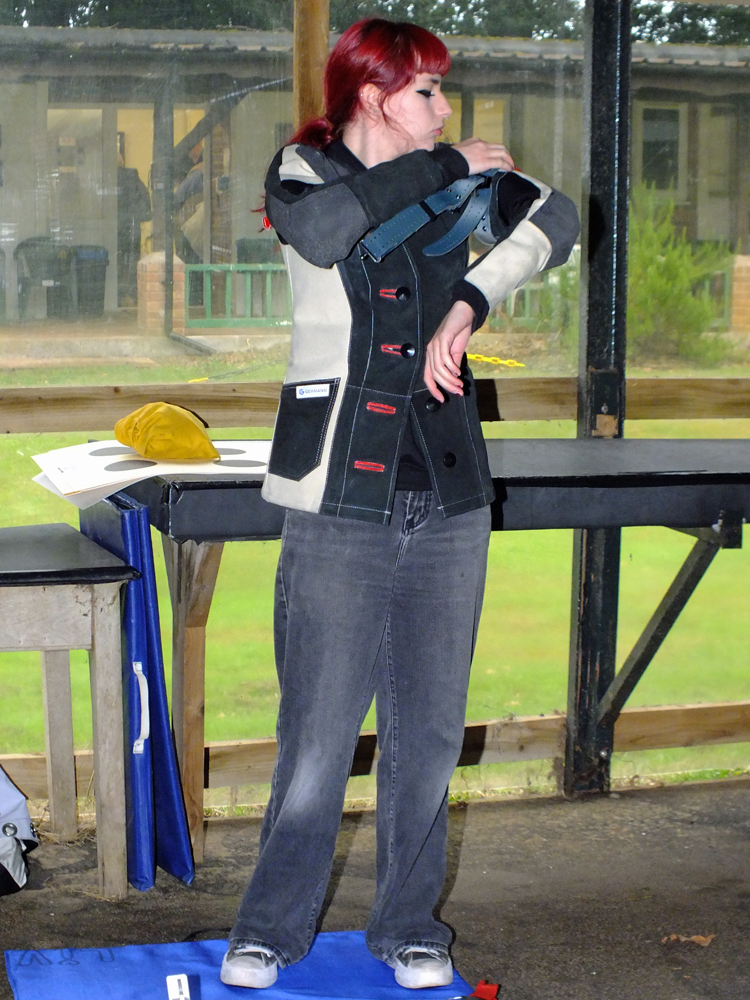 Photograph shows Olivia Kirkland on the firing line, making vital adjustments to the rifle support straps on her shooting jacket.