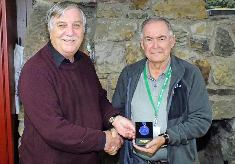 Photograph shows John Machin of Leek and District Shooting Centre (pictured right) receiving his SSRA Individual 10 Metres Air Pistol - 'B' League - Summer 2026 - 2nd Place Medal from Osborn J Spence of Leek and District Shooting Centre (pictured left).