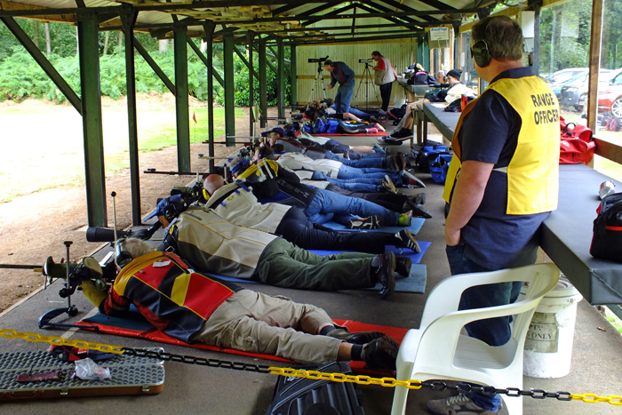 Photograph shows competitors giving it their all on the firing line, in the company of the Range Officers.