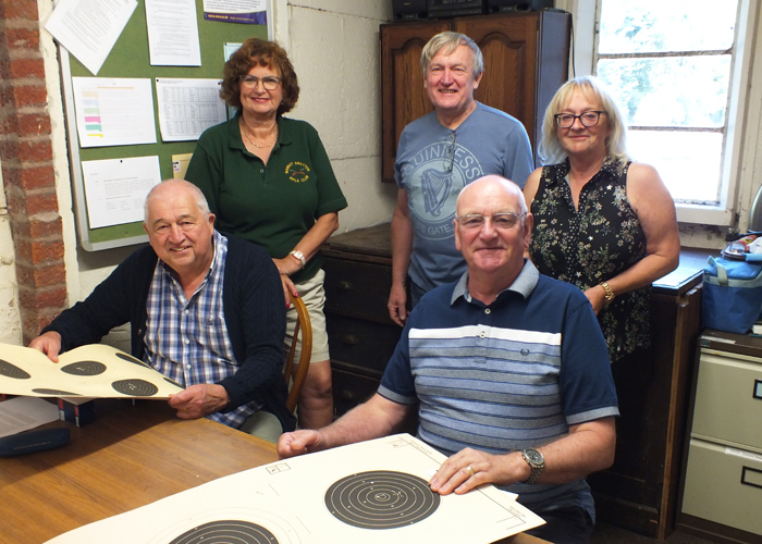 Photograph shows Judith Simcock (pictured standing left), Alan Boyles (pictured standing centre), Debbie Round (pictured standing right),  with John Wilshaw (pictured seated left) and Jeff Hickson (pictured seated right), all gathered in the official scoring room checking targets..