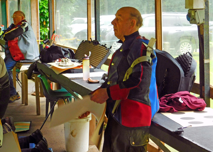 Photograph shows Brian Parker in the preparation area of the firing line, getting ready to change his target.