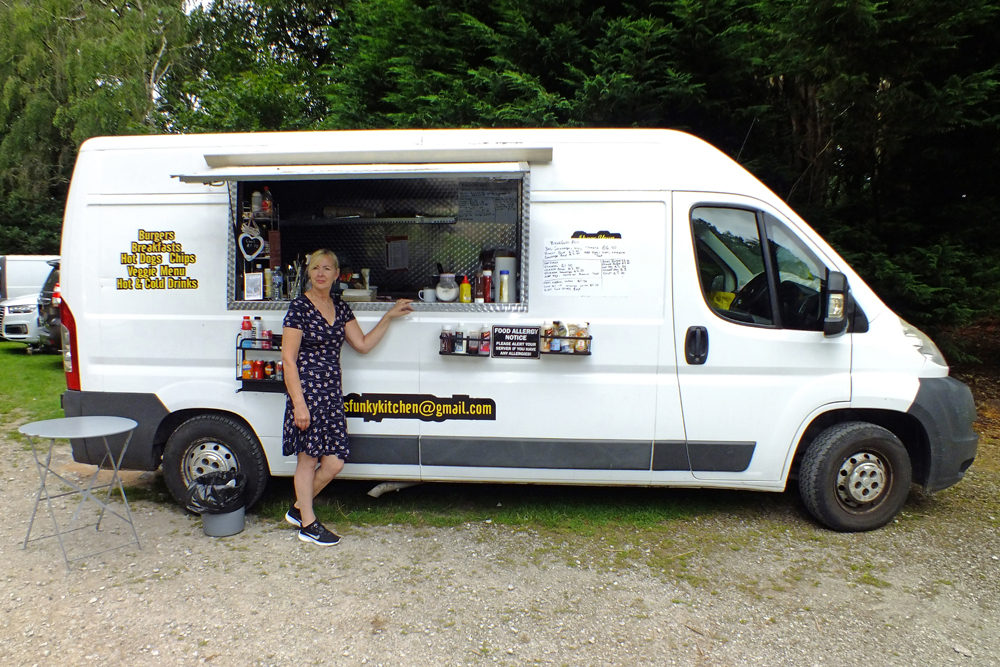 Photograph shows Sandra Williams, proprietor of San's Funky Kitchen, standing proudly alongside her treasured catering van.