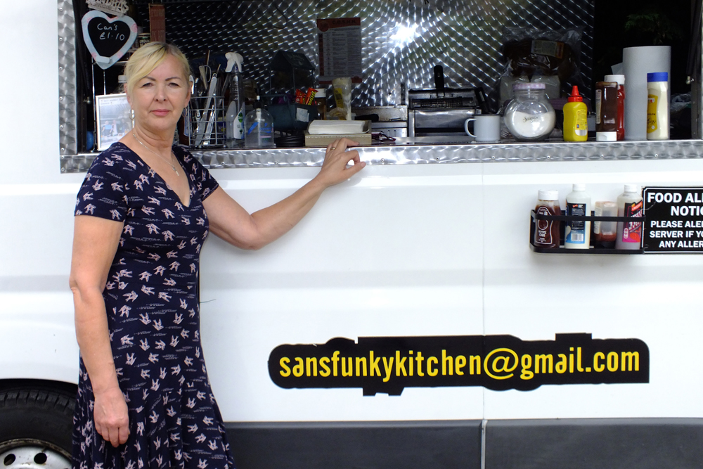 Photograph shows Sandra Williams, proprietor of San's Funky Kitchen, displaying the immaculately presented customer serving area of her van.