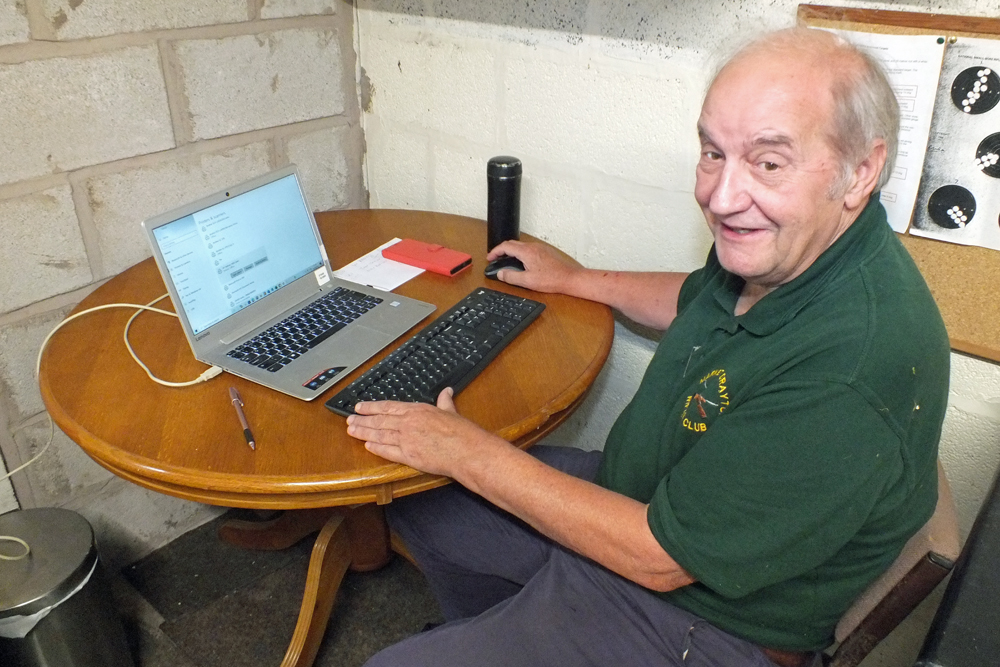 Photograph shows Bob Heath, taking over Debbie Round's duties for a while, and inputting the scores on the laptop.