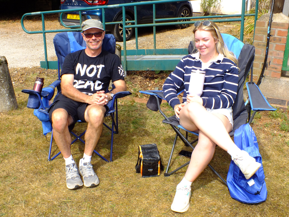 Photograph shows the ever-present cheery smiles of folks sitting in the sunshine as they await the conclusion of the day's events.