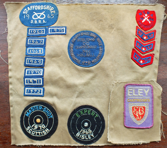 Photograph shows the back panel of a shooting jacket, bearing various shooting related badges.